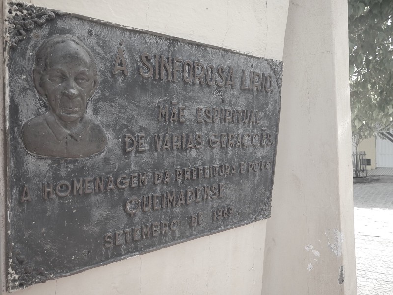 Placa em homenagem à Sinforosa numa praça. Raimunda acha que a imagem da mãe ficou parecida com a de um homem